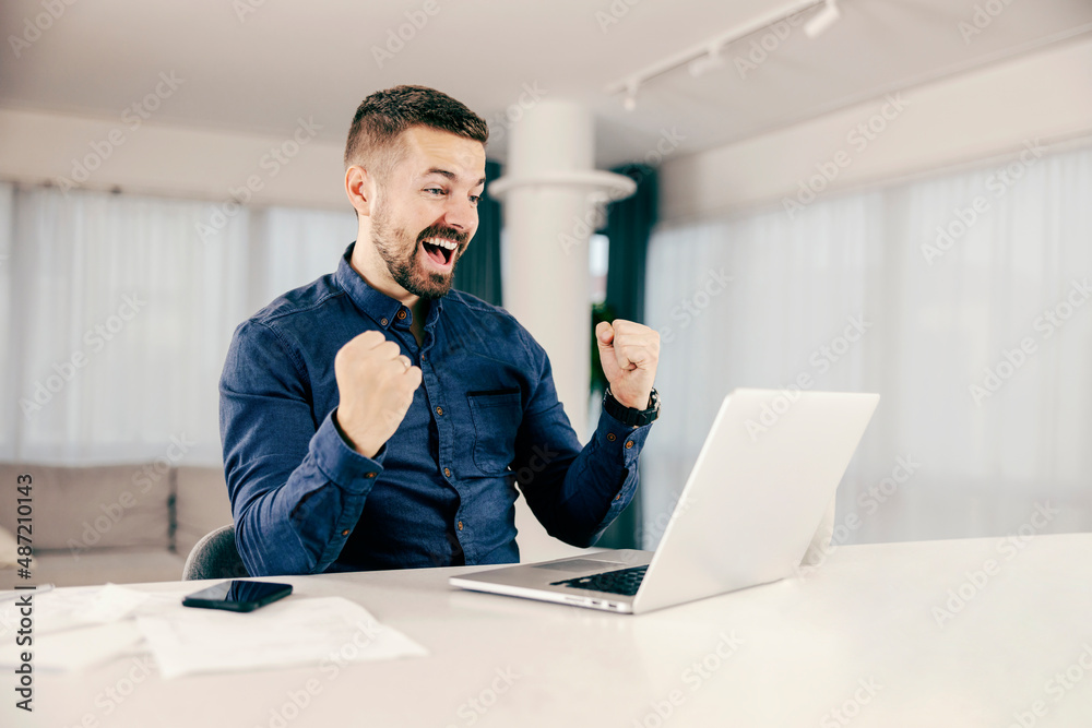 A man celebrating success while looking at the laptop from his home.