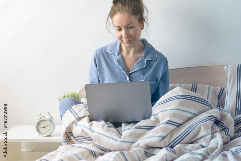 Young woman working in her pyjama from home from her bedroom in the morning. Checking mails, making conference calls, shopping online. Copy space for text Young woman working in her pyjama from home from her bedroom in the morning. Checking mails, making conference calls, shopping online. Copy space for text
