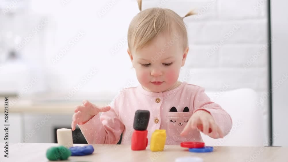 Cute Little girl with funny ponytails on head sitting in kitchen and playing multicolored plasticine, 2 years Kid girl having fun with modeling clay at home, Early education and development Cute Little girl with funny ponytails on head sitting in kitchen and playing multicolored plasticine, 2 years Kid girl having fun with modeling clay at home, Early education and development