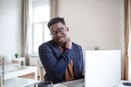 Feeling exhausted. Frustrated young handsome man looking exhausted while sitting at his home and working on his laptop while massaging his neck, Neck pain