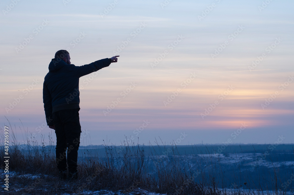 Fototapeta premium Silhouette of a man against the backdrop of sunset, sky. Man pointing his finger