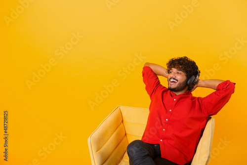 Studio portrait of relaxed cheerful indian man wearing and holding wireless headphones isolated on orange wall, enjoying listening to favorite music soundtrack, wellbeing. Meditation concept © Vadim Pastuh