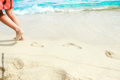 A Beach travel - woman relaxing walking on a sandy beach leaving footprints in the sand. Close up detail of female feet on golden sand at a beach in Greece. Background.