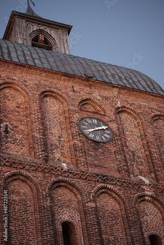 An einem großen kirchlichen Backsteingebäude prankt eine Turmuhr.
 photo
