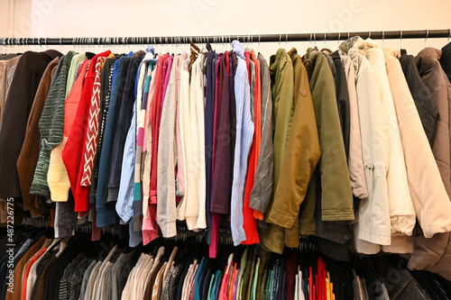 Colorful clothes hanging on a hanger for sale in shop. Clothes hanging on rack in second hand store. Shirts, T-shirts, sweaters, blouses in clothing store. photo