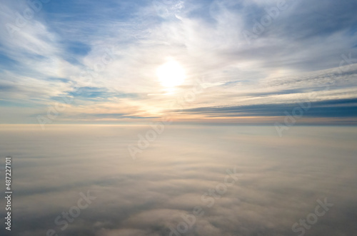 Aerial view of vibrant yellow sunrise over white dense clouds with blue sky overhead. © bilanol