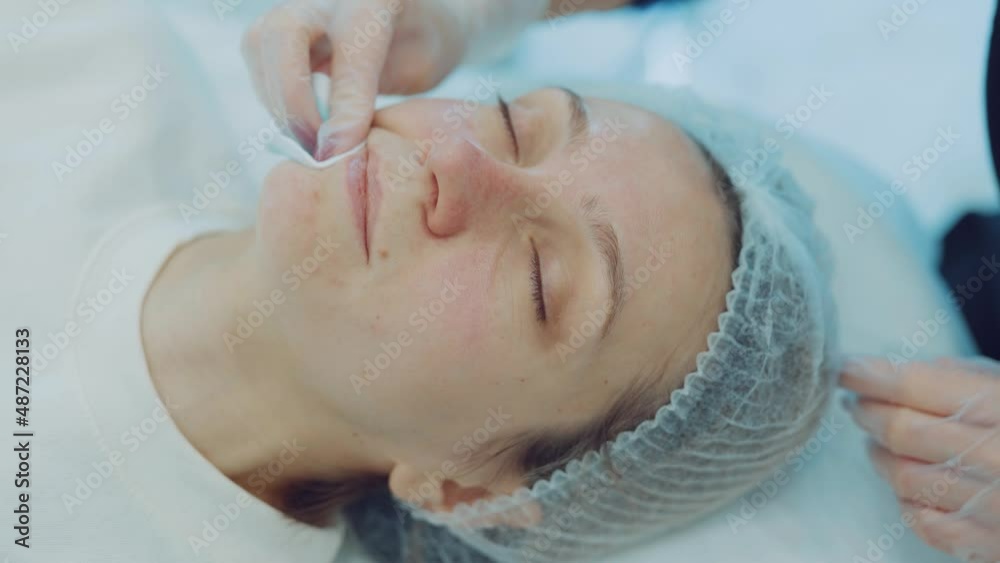 Cosmetologist cleans client's face with cotton pad. Beautician making beauty skincare procedure Cosmetologist cleans client's face with cotton pad. Beautician making beauty skincare procedure