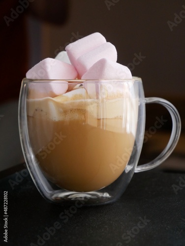 A glass cup of coffee with pink marshmallows in it