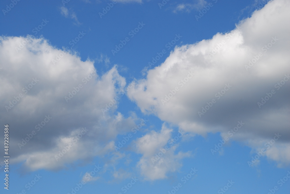 White cumulus clouds float across the sky. On a sunny summer day, snow-white fluffy cumulus clouds float across the blue sky. Clouds of different shapes and sizes below are slightly gray. White cumulus clouds float across the sky. On a sunny summer day, snow-white fluffy cumulus clouds float across the blue sky. Clouds of different shapes and sizes below are slightly gray.