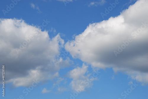 White cumulus clouds float across the sky. On a sunny summer day, snow-white fluffy cumulus clouds float across the blue sky. Clouds of different shapes and sizes below are slightly gray.