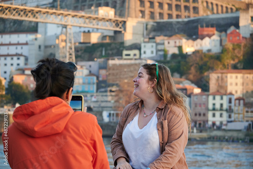 A young woman in a vibrant jacket taking a photo of her beautiful friend while traveling