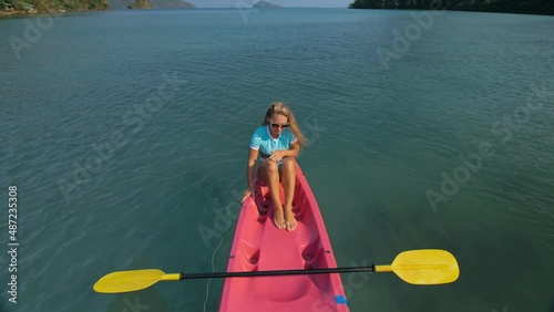 Pretty slim woman in elegant swimsuit lies in pink plastic kayak drifting on azure ocean at exotic resort upper view. Traveling to tropical countries. Girl is sailing on kayak in ocean, view above. photo