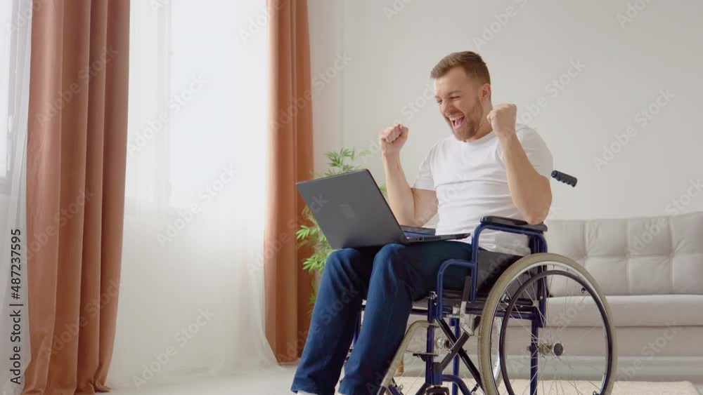 Cheerful happy disabled person rejoices at good news while sitting in wheelchair with laptop. Life of a disabled person Cheerful happy disabled person rejoices at good news while sitting in wheelchair with laptop. Life of a disabled person
