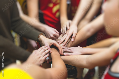 Team of kids children basketball players stacking hands in the court, sports team together holding hands getting ready for the game, playing indoor basketball, team talk with coach, close up of hands © tsuguliev