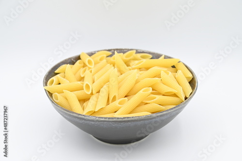 Raw penne rigate pasta, in a dark grey bowl, isolated on a white background
