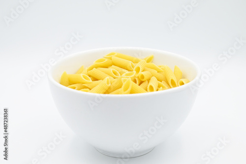 Raw penne rigate pasta, in a white bowl, isolated on a white background
