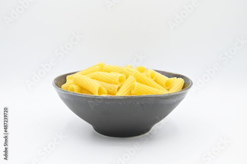 Raw Tortiglioni pasta, in a dark grey bowl, isolated on a white background
