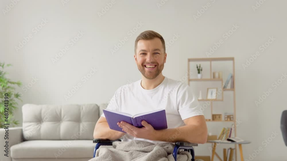 Cheerful happy disabled person reading a book in a wheelchair and looking at camera Cheerful happy disabled person reading a book in a wheelchair and looking at camera