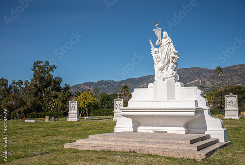 Santa Barbara, California, USA - February 8, 2022: Calvary Cemetery. Landscape with central white main statue of Jesus the savior and punisher on green burial lawn under blue sky. Santa Ynez mountains