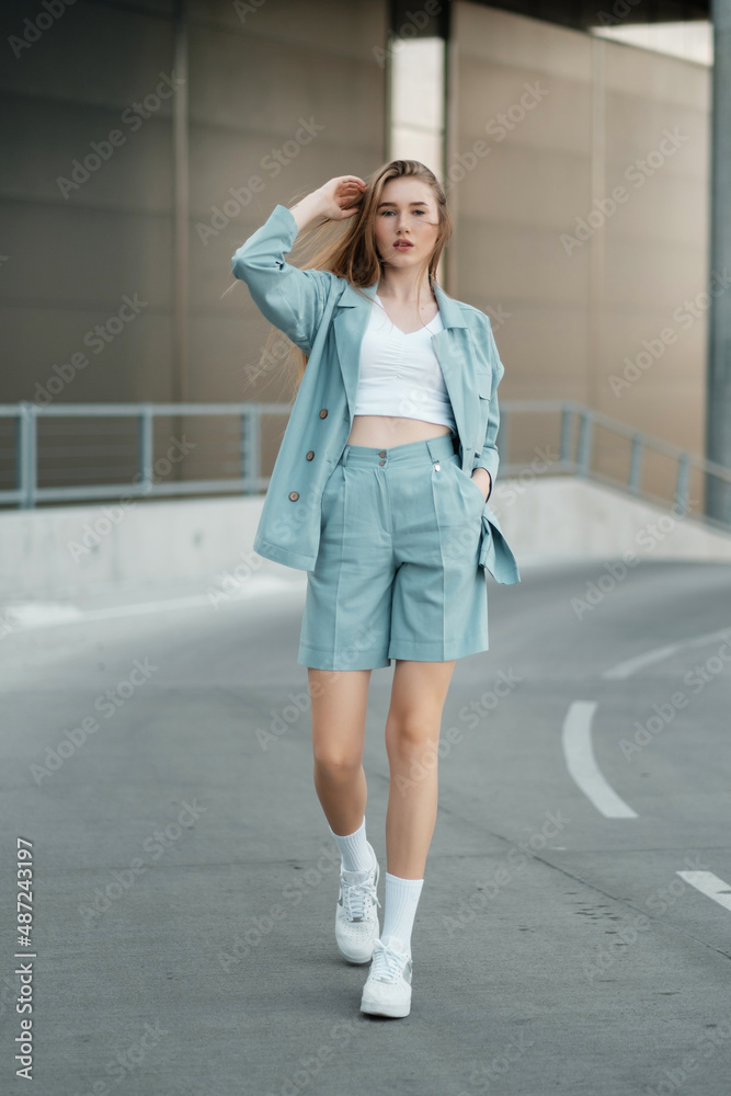 A girl with long hair in blue shorts and a jacket walking in downtown.