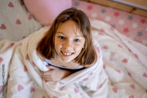 Girl woke up in her bed early in the morning and smiles. White bed linen with hearts