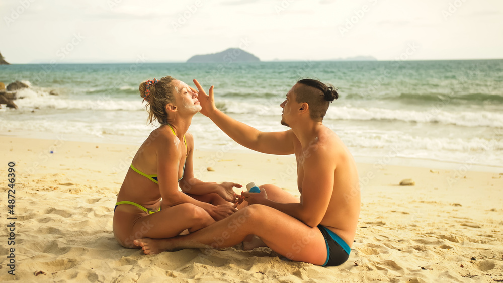 Fototapeta premium Cute loving couple each other having sun block. Woman to put sunscreen man. Young girl and guy face to face using sun cream. Concept rest tropical resort, traveling tourism happy summer holidays