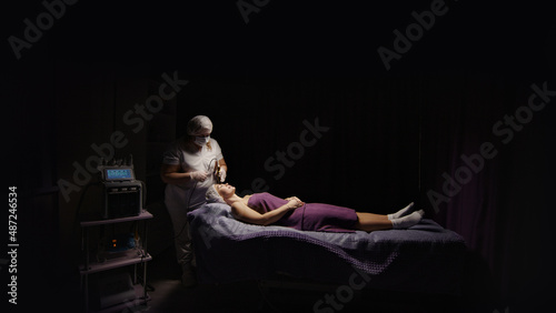 Attractive woman receiving anti-ageing anti-cellulite face massage vacuum rf lifting, spa salon. Wellness body, skin care, face beauty treatment, rejuvenation procedure. Black dark background