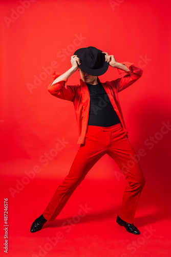 Tall handsome man dressed in red shirt and black hat posing on the red background