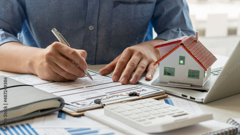Fototapeta premium People calculate interest, taxes, and profits to invest in real estate and home purchases. Real estate agents with home layouts are talking to clients about purchasing home insurance.