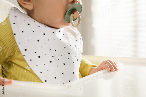 Tableau sur toile Cute little baby wearing bib in highchair indoors, closeup