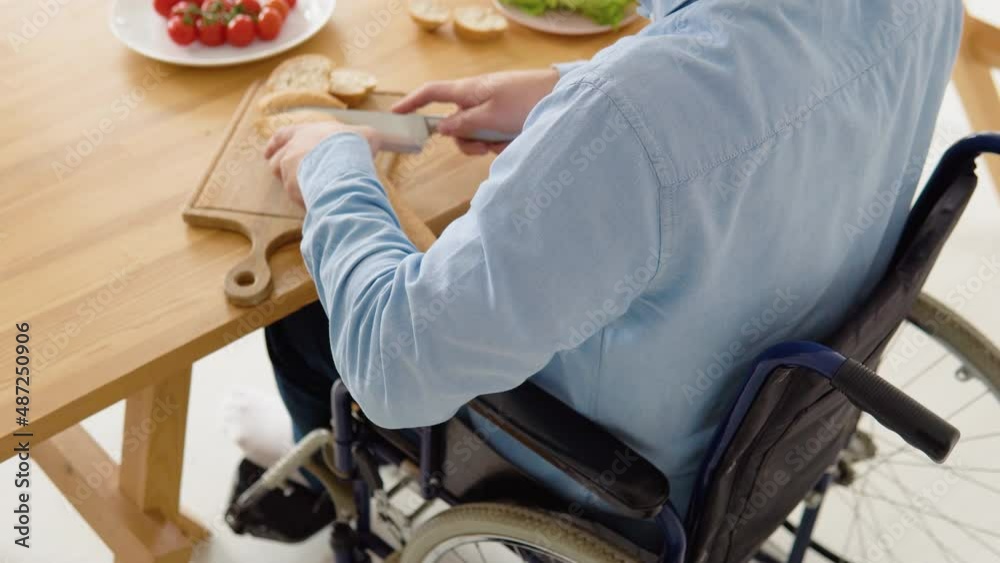 Close-up shot of a disabled person in a wheelchair cutting bread in the ...