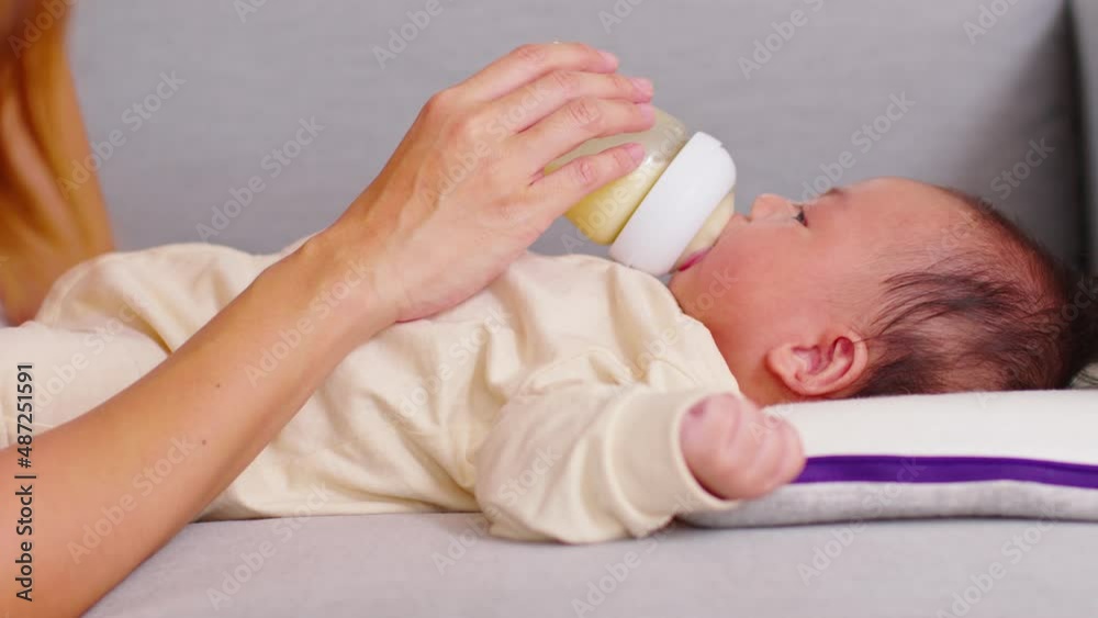 Close up hand of mother holding milk bottle Newborn baby lying on bed drinking milk.Cute infant baby feeding milk with love at home.Newborn Baby Concept Close up hand of mother holding milk bottle Newborn baby lying on bed drinking milk.Cute infant baby feeding milk with love at home.Newborn Baby Concept