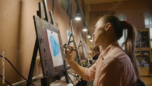 Woman artist learns to paint with airbrush with acrylic dye, paper and easel. Indoors. Concept modern art, airbrushing, aerography, draw spraying picture create sprayer drawing graffiti aerosol spray