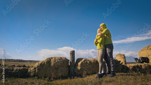 Man and woman in yellow green sportswear. Lovely couple of travelers hug and kiss near old stone enjoying highland landscape. Two travelers are walking against the backdrop of snow-capped mountains.