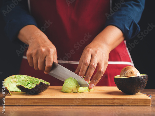 Chef slicing avocado on a wooden cutting board with the knife
