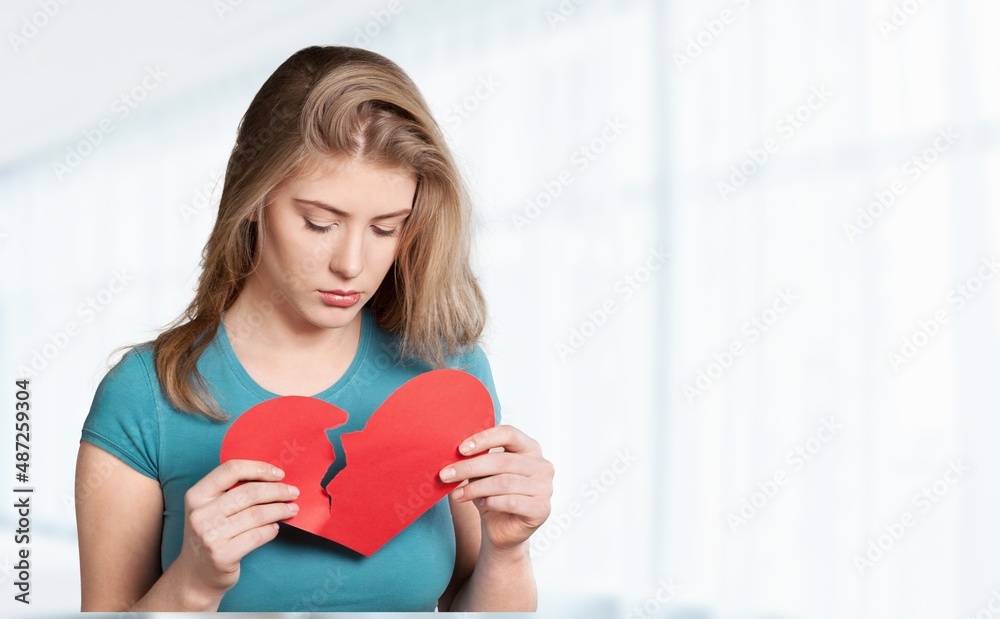 Young unhappy girl sitting near the table with broken paper heart Young unhappy girl sitting near the table with broken paper heart
