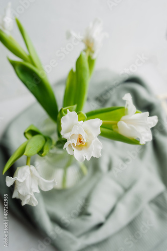 Fototapeta Naklejka Na Ścianę i Meble -  selective focus a bouquet of small white openwork tulips with green stems in a transparent vase in a cozy atmosphere. spring mood, floral content