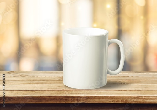 White mug on a wooden background with bright lights in the background. New Year and Christmas.