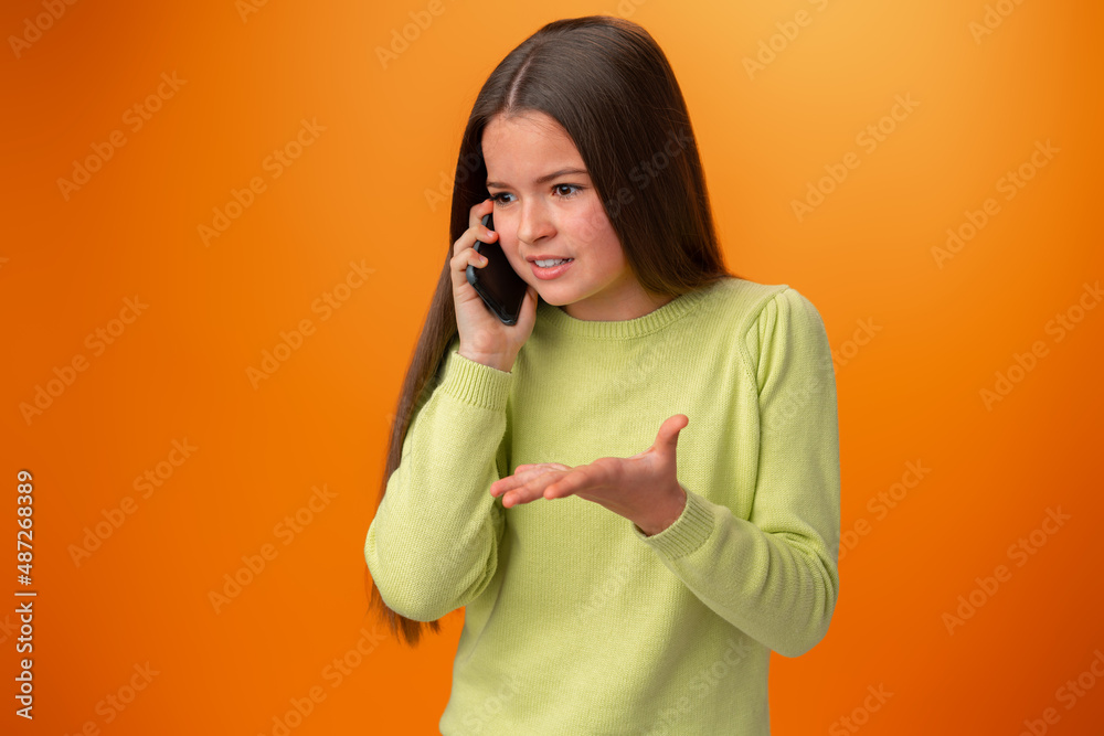 Teen girl talking on cell phone isolated on orange background Teen girl talking on cell phone isolated on orange background