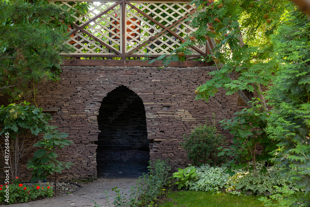 Arched door in a stone wall surrounded by greenery. Arch entrance in the stone wall. Green vegetation around