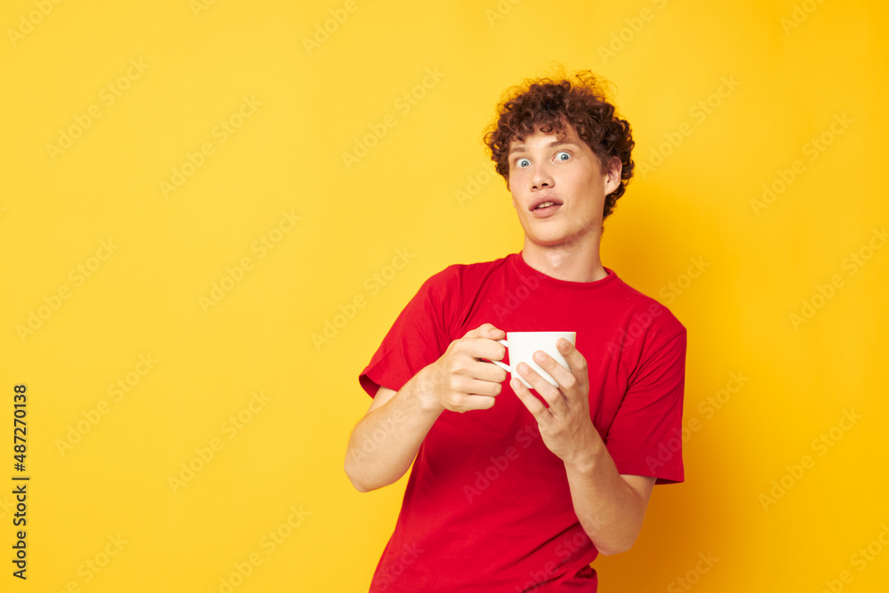 portrait of a young curly man in a red T-shirt with a white cap in his hands isolated background unaltered