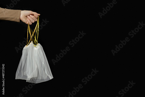 Hand holding reusable grocery bags from net, reusable packaging for fruits and vegetables, empty eco mesh bag with ribbon ties, eco friendly and zero waste concept, minimal style, side view photo