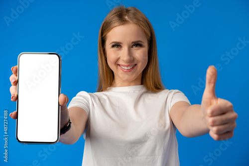 Young woman point finger at isolated smartphone screen over blue color background