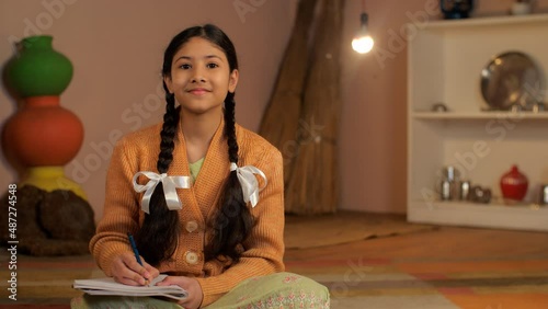 A young schoolgirl of an Indian village studying alone under an electric bulb - Beti Bachao Beti Padhao  girl education  girl portrait . A sweet girl with braided hair completing school homework - ... photo