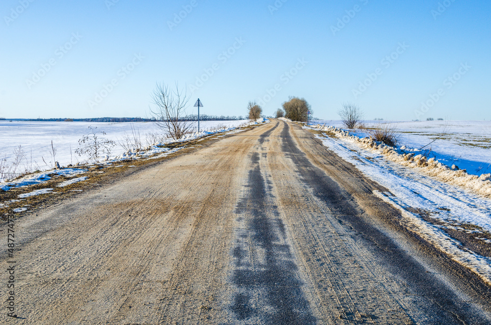 Winter road covered with sand. Asphalt road going into the distance in winter Winter road covered with sand. Asphalt road going into the distance in winter