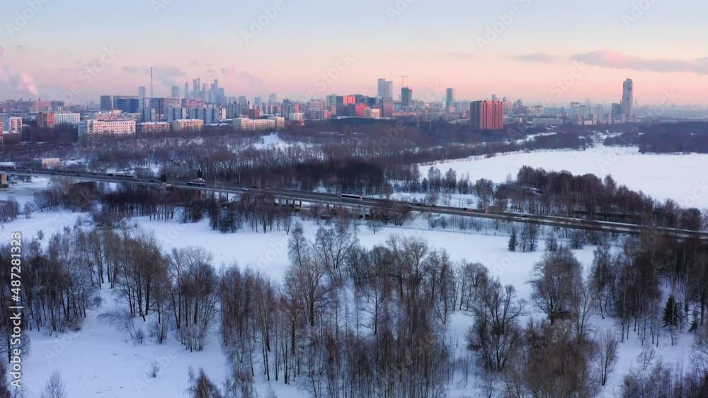 Aerial View Of Snowy Natural Parkland And Elevated Road Over It Against Built Up Urban Skyline Aerial View Of Snowy Natural Parkland And Elevated Road Over It Against Built Up Urban Skyline