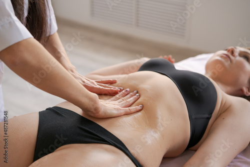Close-up on belly woman having anti-cellulite massage session with madero therapy, professional therapist holding wooden tools in studio or salon with copy space photo