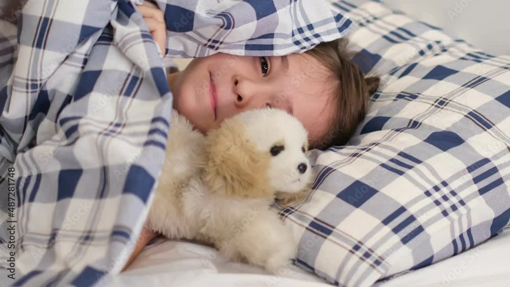 Boy hiding under the covers, peeking out. playful child does not want to get out of bed