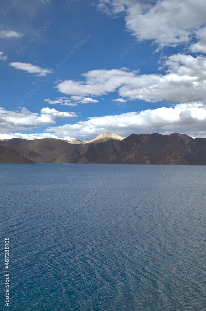 A view of Pangong Tso lake at sunset with Himalayas in the background and cloudy sky, Ladakh, India.