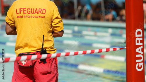 A public pool life guard or pool safety officer in uniform standing duty or guard supervising swimming and children preventing drowning accidents.